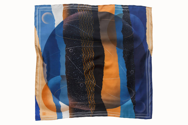 Flatlay image of 100% silk square scarf featuring a cosmic collage motif, including a large planet in the center surrounded by the moon phases and stars in outer space. Colors used include shades of warm oranges and blues as well as white and black details.