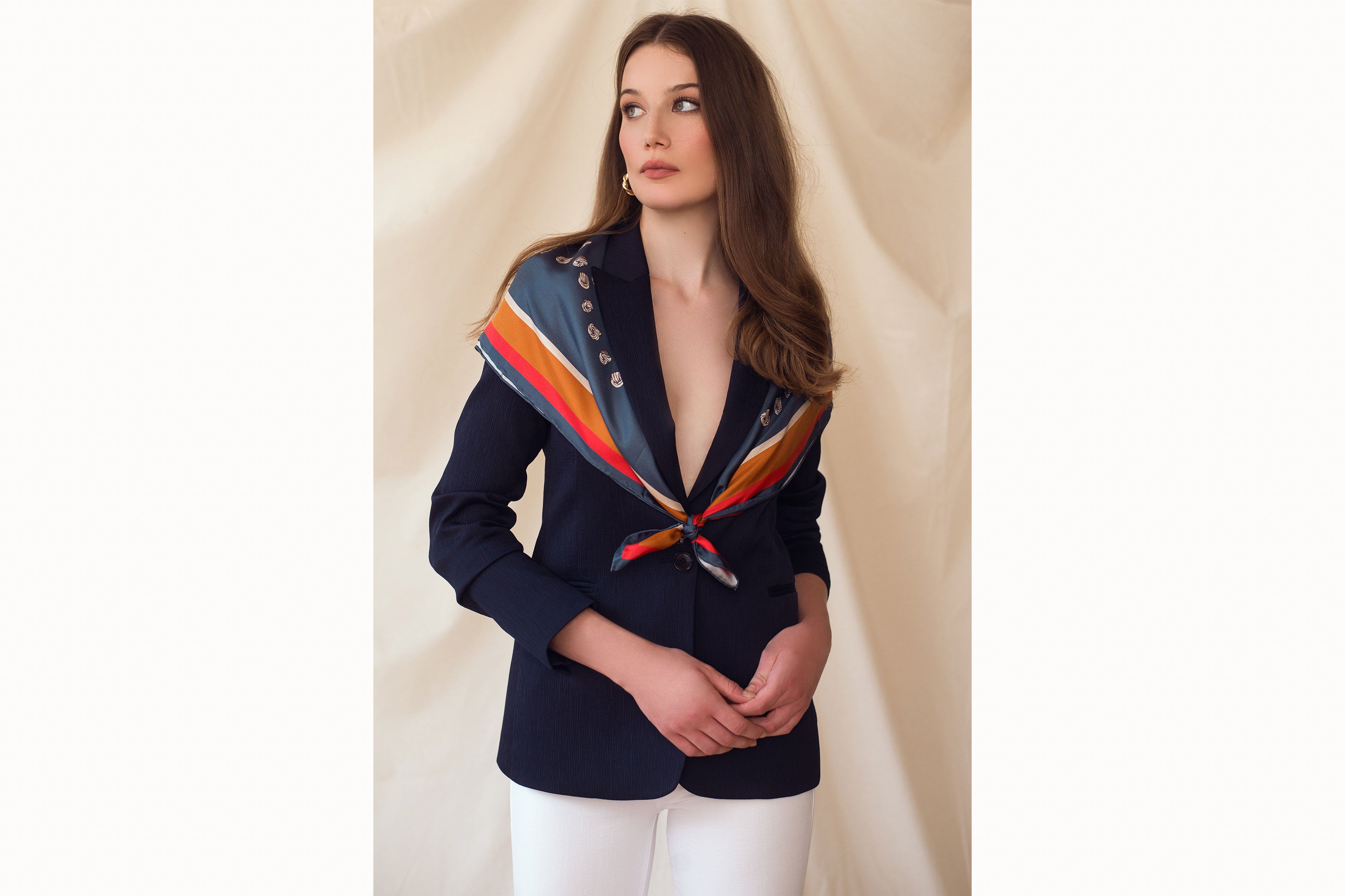 Image of female model wearing the scarf folded in half on the diagonal and wrapped around her shoulders tied in a low knot in front. The model is also wearing a navy blazer.